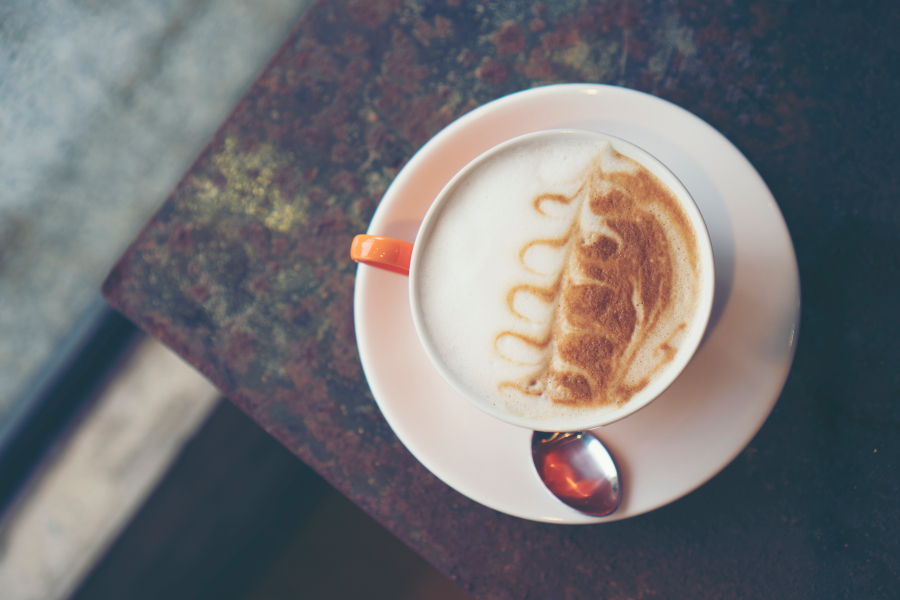 Kaffee mit Milchschaum und Latte-Art in einer Tasse auf Untertasse, von oben fotografiert.