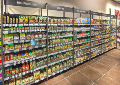 BioabteilLanges Supermarktregal mit Bio-Produkten, beschriftet „Bio-Produkte“ und „Demeter“, voll mit verpackten Lebensmitteln.ung