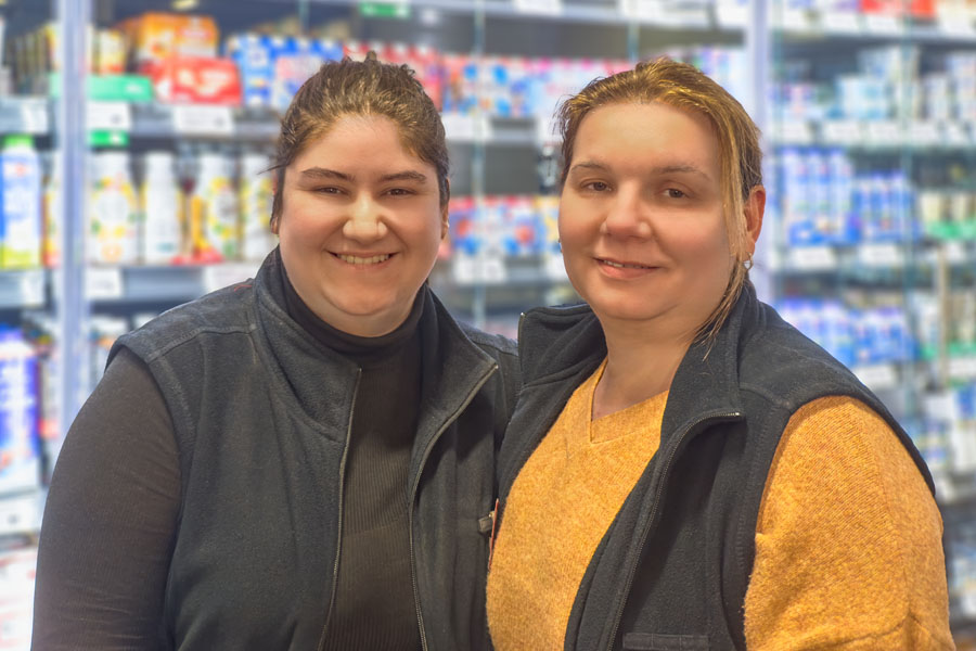 Zwei Frauen lächeln vor einem Supermarktregal mit Milchprodukten.